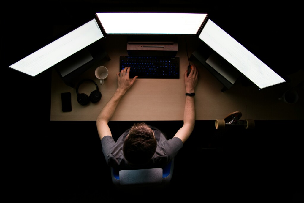 man sitting in front of 3 computer screens typing